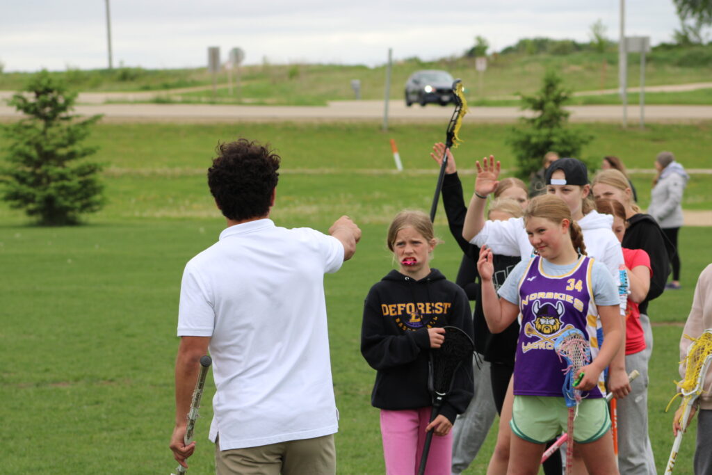 Devon Townsend coaching a youth skills group during an X Factor Lacrosse session, giving hands-on instruction and encouragement on the field